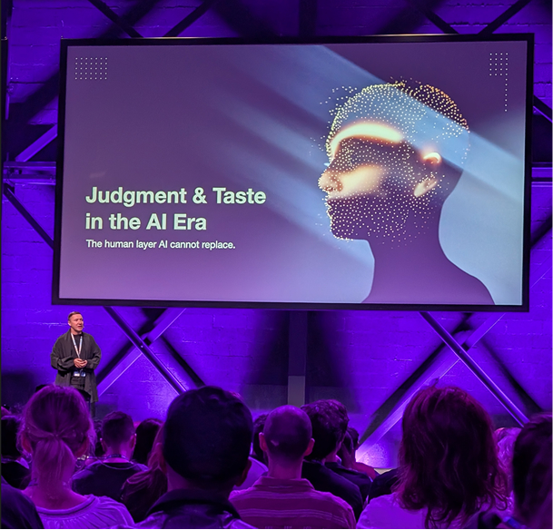 Speaker vor großer Leinwand mit der Folie ‚Judgment & Taste in the AI Era‘