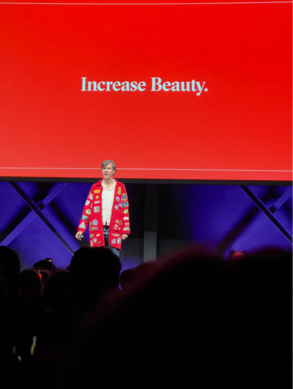 Speaker auf der Bühne vor roter Folie mit dem Text ‚Increase Beauty'