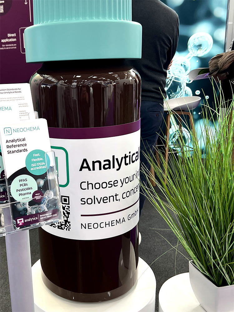 Großes Produktmodell (Flasche) am Messestand mit NEOCHEMA-Label und Prospekthalter