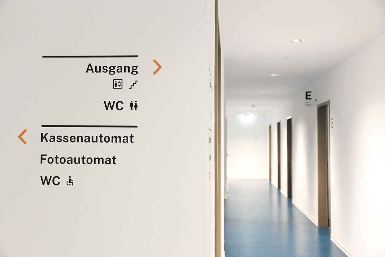 Wand mit Wegweisern für Ausgang, WC und Kassenautomat in einem Flur