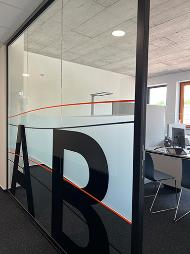 Glaswand mit dem Schriftzug A+B und einem Büro im Hintergrund