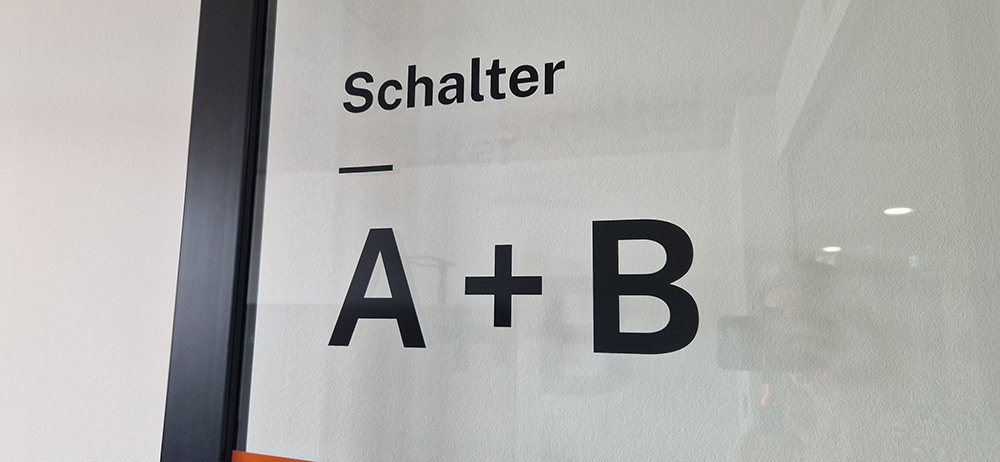 Glaswand mit dem Schriftzug Schalter und A+B