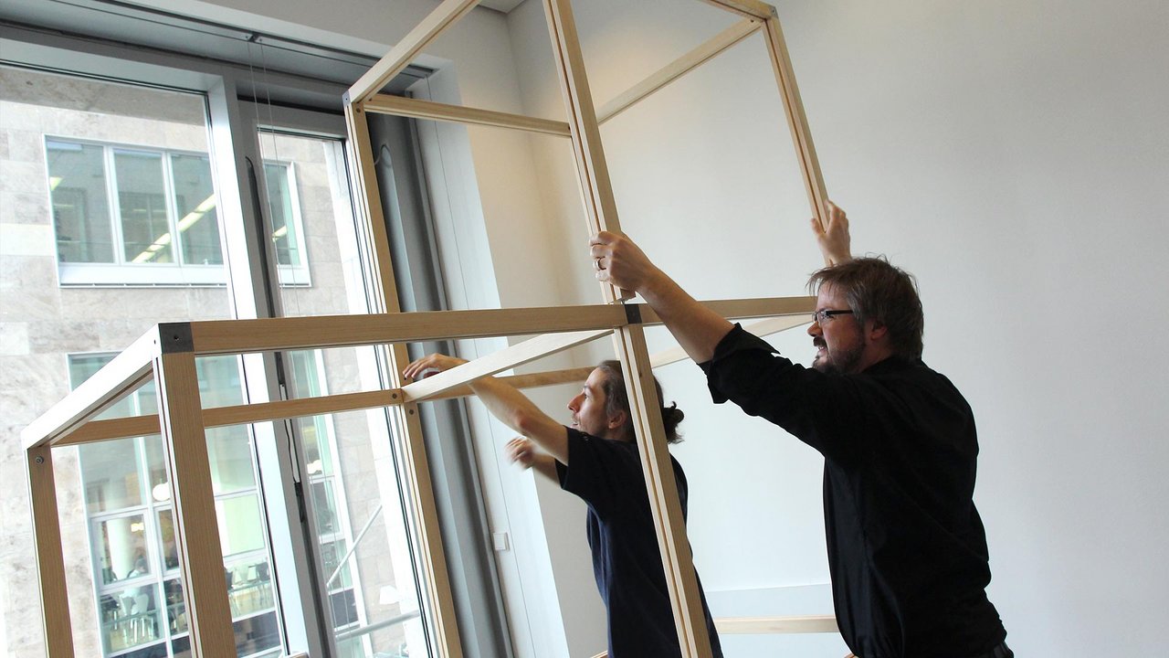 Zwei Personen montieren ein modulares Ausstellungssystem aus Holzrahmen