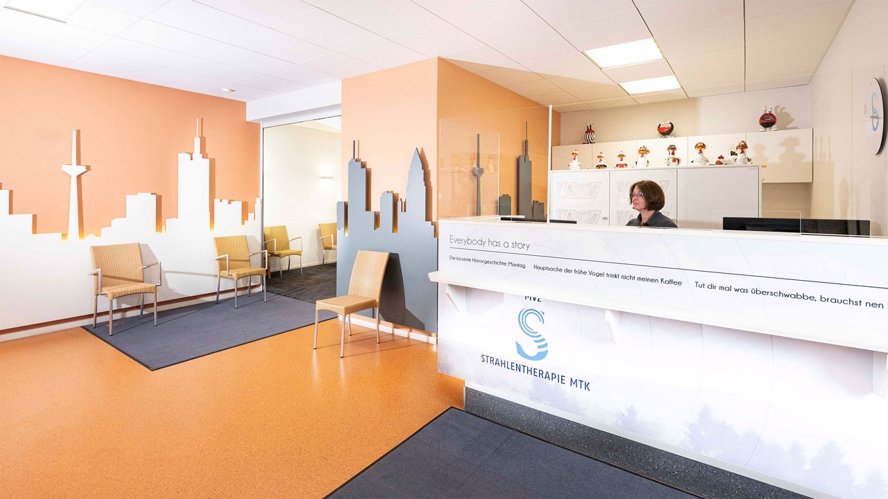 Praxisraum von MTK Strahlentherapie mit Empfangstresen, Sitzbereich und orangefarbenem Boden